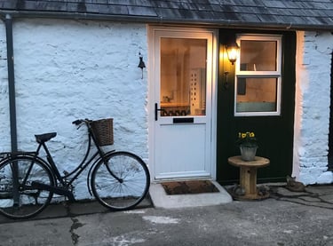White door and shop front, an old bicycle leaning against the wall. The lights are on inside.