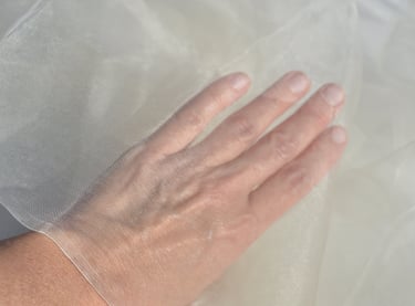A person's hand touching fine white sheer organza fabric, showcasing its delicate mesh texture.