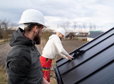 Professional roofing contractors in hard hats installing a black metal roof on a residential house.