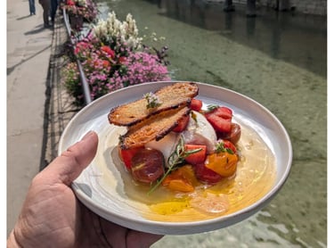 Une personne tient une assiette avec une burratta accompagné de fraises, tomates et un croustillant