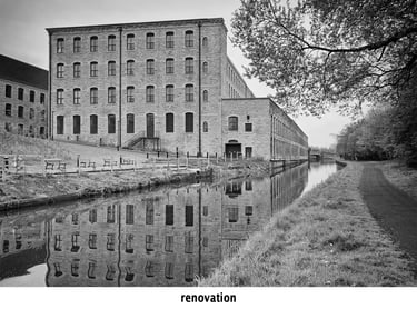 a black and white photo of a renovated building with a reflections in the canal