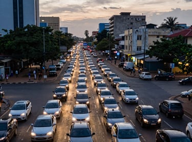 A high-angle view of a busy Abidjan intersection at sunset, showing a dense gridlock of cars with glowing headlights. The urban landscape includes modern buildings and tropical greenery. The mood is tense, highlighting the challenge of rapid ground response. Professional photography in medium blue and warm light tones.