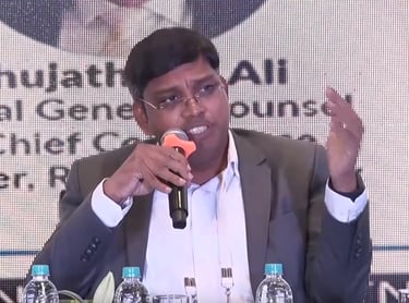 a man in a suit and glasses speaking into a microphone