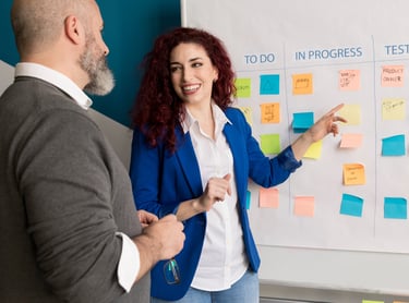 a man and woman standing in front of a white board with sticky notes on it