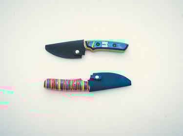 Two handmade fixed blade knives with colorful striped recycled skateboard wood handles and leather sheaths.