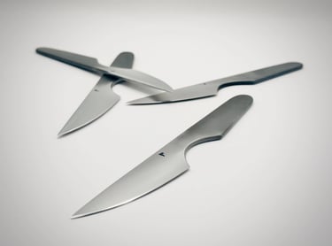 Three minimalist stainless steel steak knives with ergonomic handles on a white background.