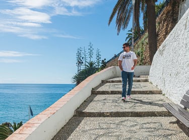 A man walks down a scenic cobblestone coastal path in Spain overlooking the Mediterranean Sea.