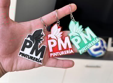 Custom 3D printed Pinturería PM logo  3d llaveros posadas in black, red, and green held in a hand.