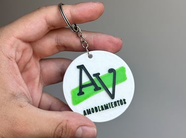Custom 3D printed round keychain with black AV logo and green accent for Amoblamientos.
