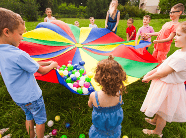 Children playing outdoors with colorful balls on a colorful blanket.