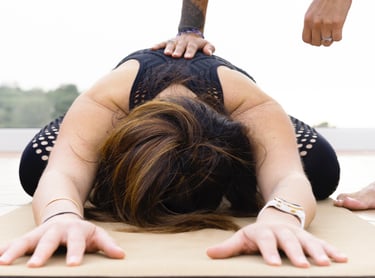 Yoga instructor providing a hands-on adjustment for a woman in child's pose on an outdoor patio mat.