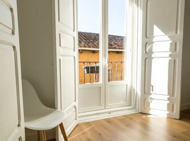Minimalist room with light oak wood floors, white shutters, and a modern chair by a sunlit window.