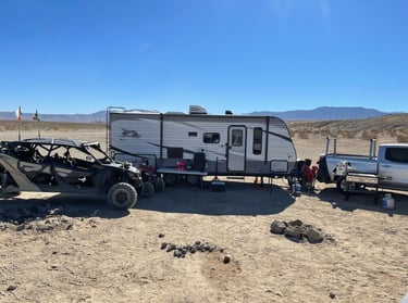 A Jayco travel trailer camper parked in the desert with an off-road UTV and a silver pickup truck.