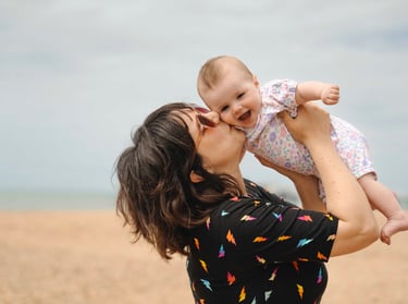Mother holding her baby in the air and kissing her cheek on the beach