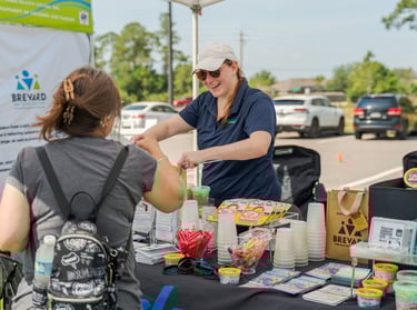 a woman is standing at a table is smiling and handing information to a person visiting the booth
