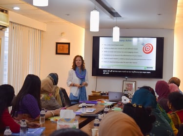 a woman in a white shirt is standing in front of a large screen talking to a room full of women