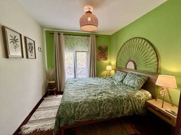 Tropical bohemian bedroom with green walls, rattan headboard, and palm leaf bedding.