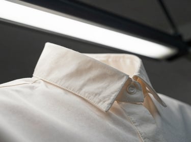 Extreme close-up of a structured women's blouse collar seam under tension on a white workbench, bright overhead fluorescent light, stitching rows visible in sharp detail, no model