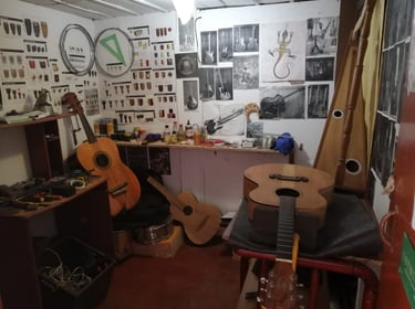 Taller de luthería con diversos instrumentos de cuerda, herramientas, moldería e imágenes en pared