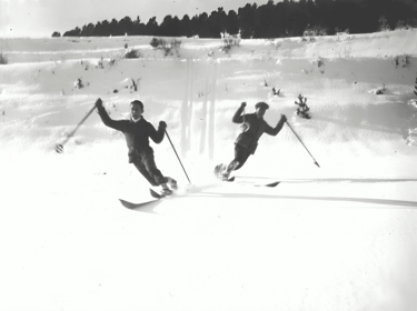 a blakc and white image of two men skiing toward the camera