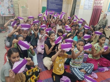 Indian girls at World Menstrual Hygiene Day sitting on the floor holding up fabric sanitary napkins.