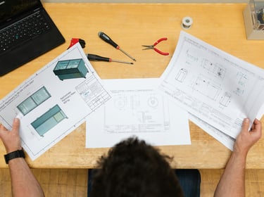 Engineer reviewing mechanical blueprints and technical drawings at an industrial workstation.