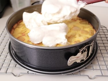 Spreading fluffy white meringue topping onto a freshly baked fruit tart in a springform pan.