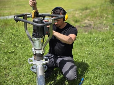 Professional technician installing a helical screw pile foundation using a portable power drive tool.