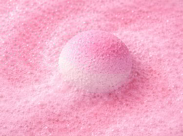 Large pink bath bomb surrounded by fluffy foam and gentle fizz.