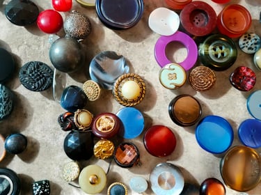 A colorful collection of vintage sewing buttons in various sizes, textures, and materials spread across a surface.