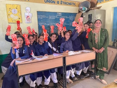 About 12 girls in classroom holding up napkin packs.