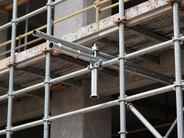 On-site construction photograph of scaffolding systems assembled on a building facade, forged couplers and ledger tubes in close detail, natural daylight, no workers visible