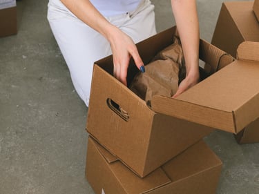Moteris pakuojanti daiktus į dėžę persikraustant
