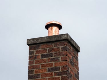 Newly installed copper chimney cap on a brick chimney, against a New England sky.