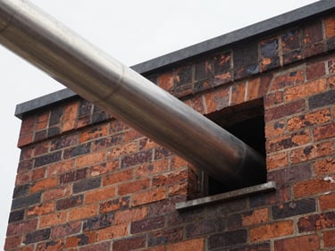 Stainless steel flue liner being lowered into a chimney, seen from above, overcast daylight.