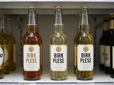 Three glass beverage bottles in a row on a white retail shelf, labels showing typographic hierarchy clearly under window light, condensation absent, honest product photography