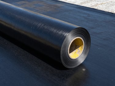 Roll of premium black bitumen waterproofing membrane on a clean concrete foundation, sharp daylight, high-contrast architectural photography, 35mm