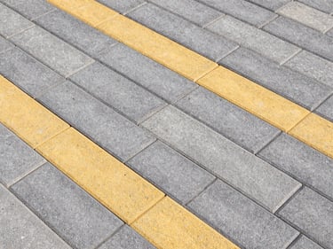 Top-down view of newly laid grey and yellow interlock paving tiles in a geometric pattern, clean joints, crisp daylight