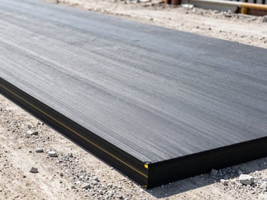 Grey geotextile membrane sheet laid out on a gravel roadbed under bright daylight, industrial construction site, sharp focus