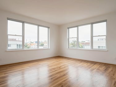 Wide interior shot of a clean two-bedroom apartment, north-facing daylight through large windows, hardwood floors visible, empty living room with white walls