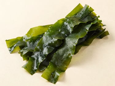 Overhead flat-lay of dried Ulva seaweed on a pale neutral surface, thin bright green sheet-like fronds, crinkled edges showing texture, bright diffused studio light, shadow-free, true color