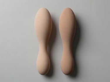 Top-down studio photograph of two masturbator sleeves placed side by side on a neutral grey-white surface, overhead hard light revealing material detail and form factor, clean background, no people, no implied use