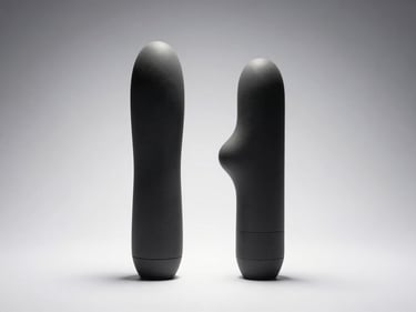 Straight-on studio shot of two compact vibrators laid flat on a clean white surface, one with a curved tip, strong overhead directional lighting revealing silicone texture and material sheen, neutral grey-white background, no people, no staging