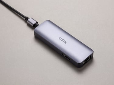 Overhead flat-lay of a USB-C to multi-port hub on a neutral matte surface, studio strobe lighting, port labels and cable detail visible, clean background, minimal shadow