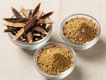 Overhead close-up of dried ashwagandha root pieces and shatavari powder in separate small glass bowls on a pale linen surface, north-facing daylight, textures clearly visible