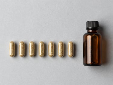 Flat-lay overhead of finished herbal supplement capsules arranged in a row beside a small labeled amber glass bottle on a neutral grey surface, bright even studio lighting