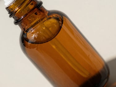 Extreme close-up overhead studio shot of a sealed amber glass bottle of herbal face serum on a neutral surface, liquid visible through glass, bright north-facing diffused studio light, clean and unhurried framing