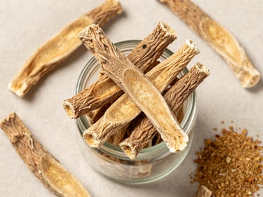 Overhead flat-lay of dried licorice root sticks and powdered extract in a small glass jar arranged on a pale linen cloth under bright diffused studio light, close-up framing showing root fiber texture
