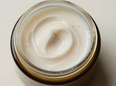 Extreme close-up overhead studio shot of a small open jar of herbal face cream on a neutral off-white surface, cream texture visible with fine botanical particulates, bright diffused daylight from above, no props