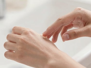 Close-up of glowing skin, gentle hands applying a soft serum, warm diffused daylight, shallow depth of field